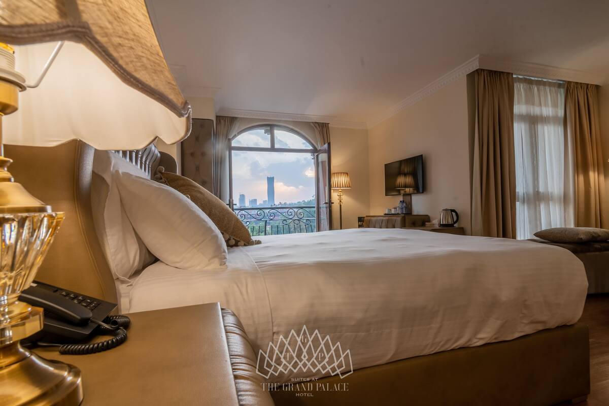 Une chambre d’hôtel avec un grand lit, un bureau avec un téléphone, une lampe et une vue sur le paysage urbain par la fenêtre.