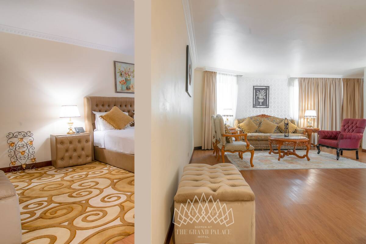 Une chambre d’hôtel avec un grand lit, un canapé, un fauteuil rouge, une petite table et un tapis à motifs.