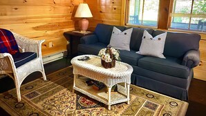 A cozy living room with a blue sofa, wicker chair, and a small table with a lamp and flowers. - Cottage by the Lake #3 - Blossoms (Bristol)