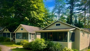 A row of single-story houses with attached porches, surrounded by lush greenery and a gravel driveway. - Cottage by the Lake #3 - Blossoms (Bristol)