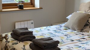 A bedroom with a bed, a bedside table, a window with a view of trees, and a thermostat on the wall. - Rural Retreat in Warwickshire (Rowington)