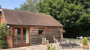 A wooden cabin with a tiled patio, two white chairs, a small table, and potted plants. - Rural Retreat in Warwickshire (Rowington)