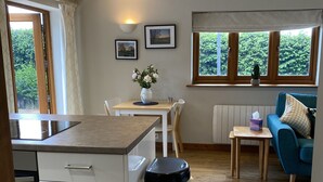 A modern kitchen with white cabinetry, a wooden countertop, and a stainless steel trash bin. There is a dining area with a table and chairs, and a blue sofa in the living area. - Rural Retreat in Warwickshire (Rowington)