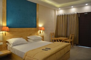 Una habitación de hotel con cama, dos lámparas de noche, una mesa, una silla y una cortina.