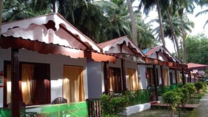 A row of small, single-story cottages with white walls and brown roofs, each with a balcony and a small garden area. - Coconhuts Beach Resort-neil Island (Port Blair)