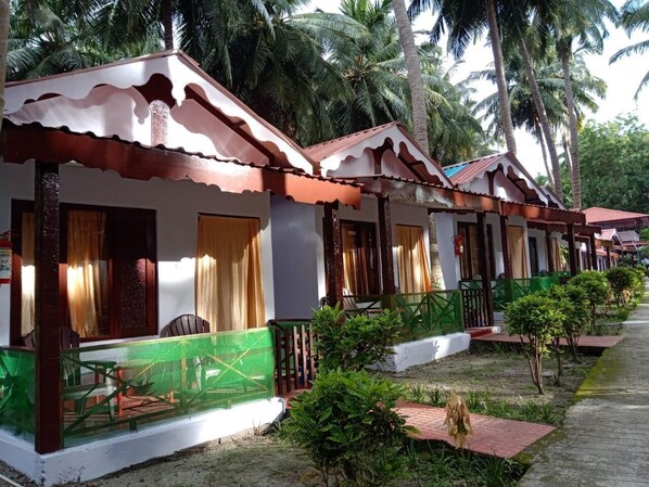 A row of small, single-story cottages with white walls and brown roofs, each with a balcony and a small garden area. - Coconhuts Beach Resort-neil Island (Port Blair)