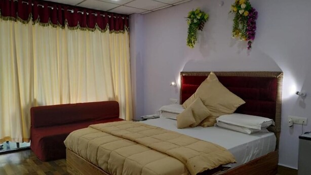 A bedroom with a bed, a bedside table, a nightstand, a red sofa, and a window with curtains. - Coconhuts Beach Resort-neil Island (Port Blair)