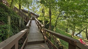 A wooden staircase leading to a building surrounded by lush greenery and a body of water. - Waterfront 4 bedroom Cabin with Outdoor Amenities (Broken Bow)