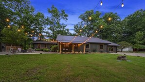 A house with a porch, surrounded by a grassy yard and trees. - Waterfront 4 bedroom Cabin with Outdoor Amenities (Broken Bow)