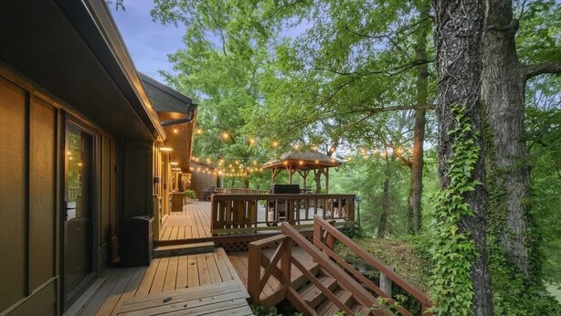 A wooden deck with a gazebo, surrounded by trees and string lights. - Waterfront 4 bedroom Cabin with Outdoor Amenities (Broken Bow)