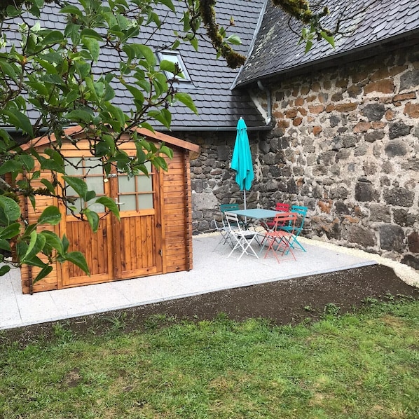 A wooden shed with a window, a stone wall, and a small patio with a table and chairs.