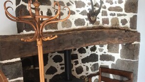 A rustic stone fireplace with a black wood-burning stove, a wooden bench, and a wrought iron coat rack.