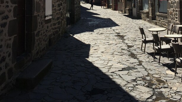 A cobblestone street lined with stone buildings, some with visible signage.