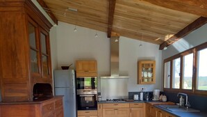 Une cuisine avec des meubles de rangement en bois, un four encastré, un réfrigérateur et un coin repas comprenant une table et des chaises en verre.