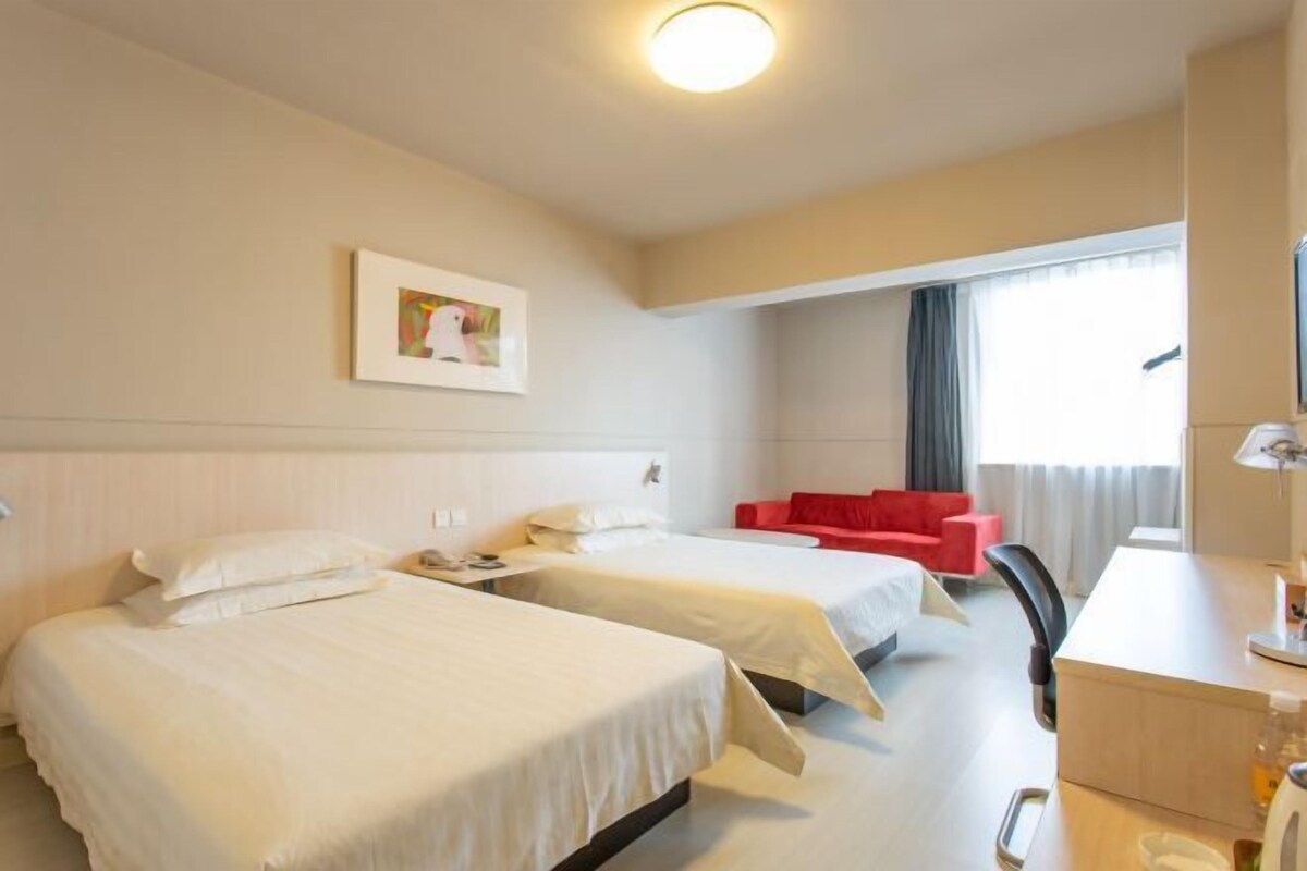 Une chambre d’hôtel avec deux lits, un bureau, une chaise, une télévision et une fenêtre avec des rideaux.