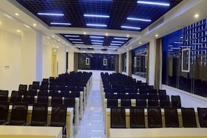Uma sala de conferências com fileiras de cadeiras, uma mesa comprida e um design moderno no teto.
