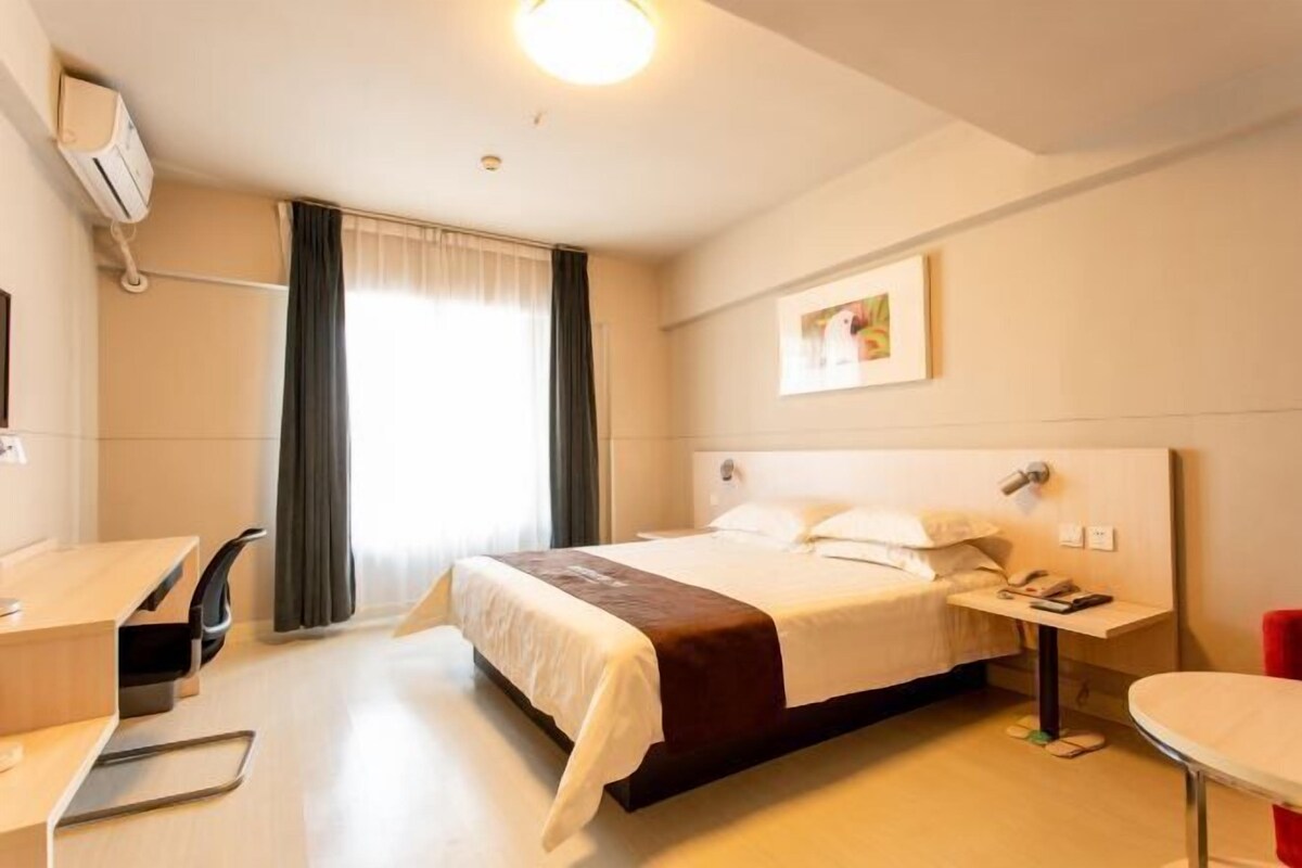 Une chambre d’hôtel comprenant un lit, une table de chevet, un bureau, une chaise et une fenêtre avec des rideaux.
