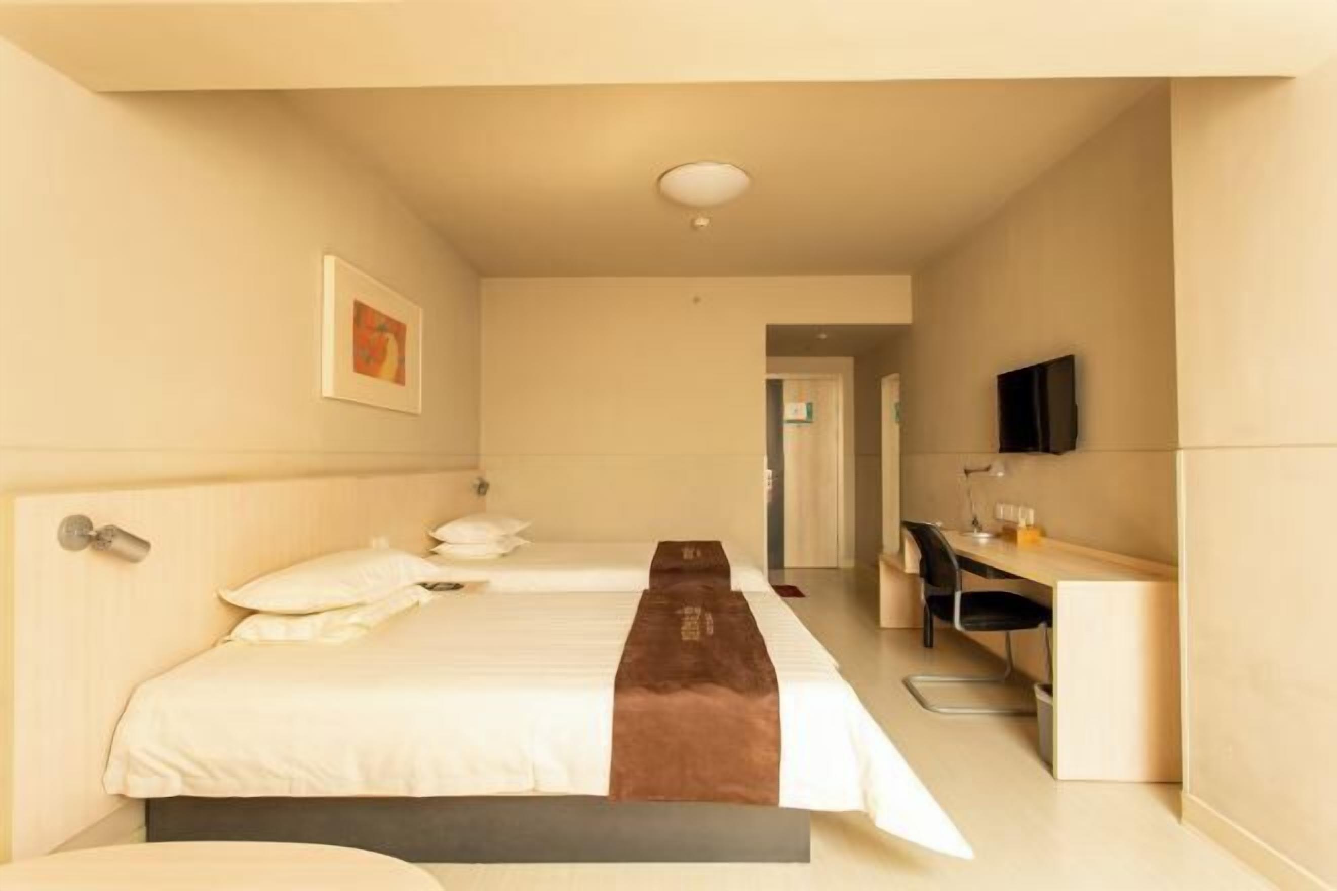 A hotel room with a bed, a desk, a chair, a television, and a framed picture on the wall.