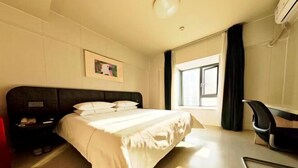 A hotel room with a bed, a desk, a chair, a window with curtains, and a wall-mounted air conditioner. - Jinjiang Inn (Xianning Yinquan Avenue) (Xianning)