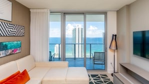 Une chambre d’hôtel moderne avec balcon, canapé, télévision et œuvres d’art aux murs.