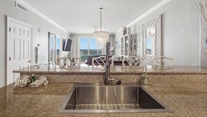 A modern kitchen with granite countertops, stainless steel sink, and a chandelier.