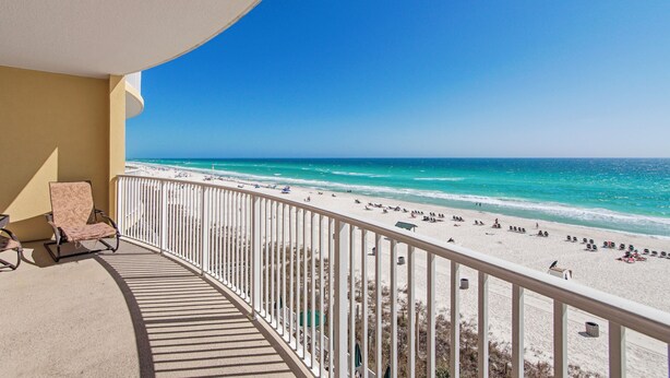 A balcony with a view of a beach, a chair, and a railing.