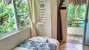A room with a bed, a window with curtains, a door leading to an outdoor area, and a view of greenery outside.