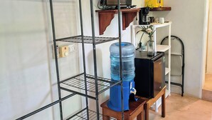 A room with a metal shelving unit, a water dispenser, a television, and a shelf with decorative items.