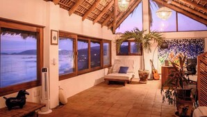 A room with a large window overlooking a body of water, a bed, a desk, and a guitar. - Lazuli Cielo - Beachfront Loft (Santa María Tonameca)