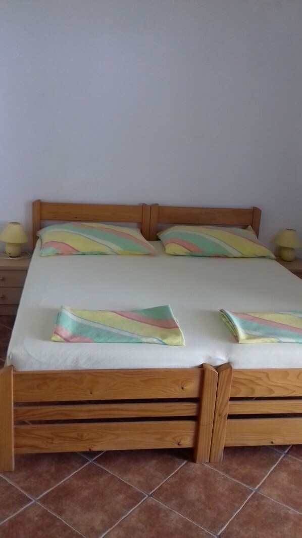 Un lit en bois avec un matelas blanc et des coussins colorés, deux lampes de chevet et un sol carrelé.