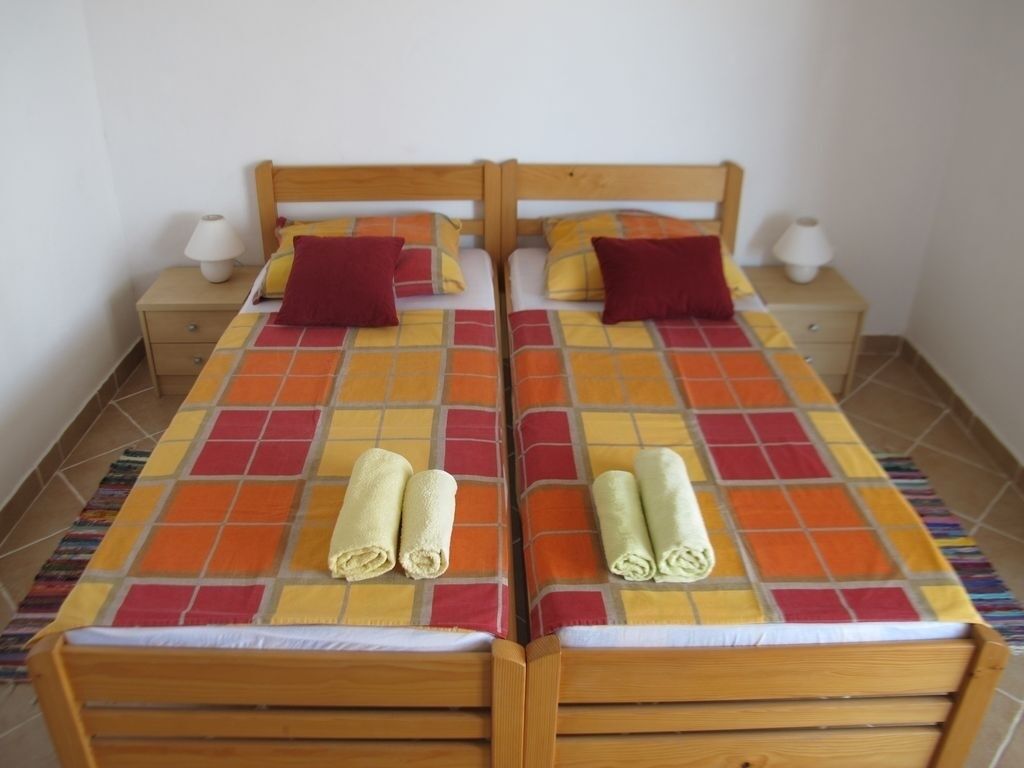 A double bed with a colorful quilt, two pillows, and two rolled towels.