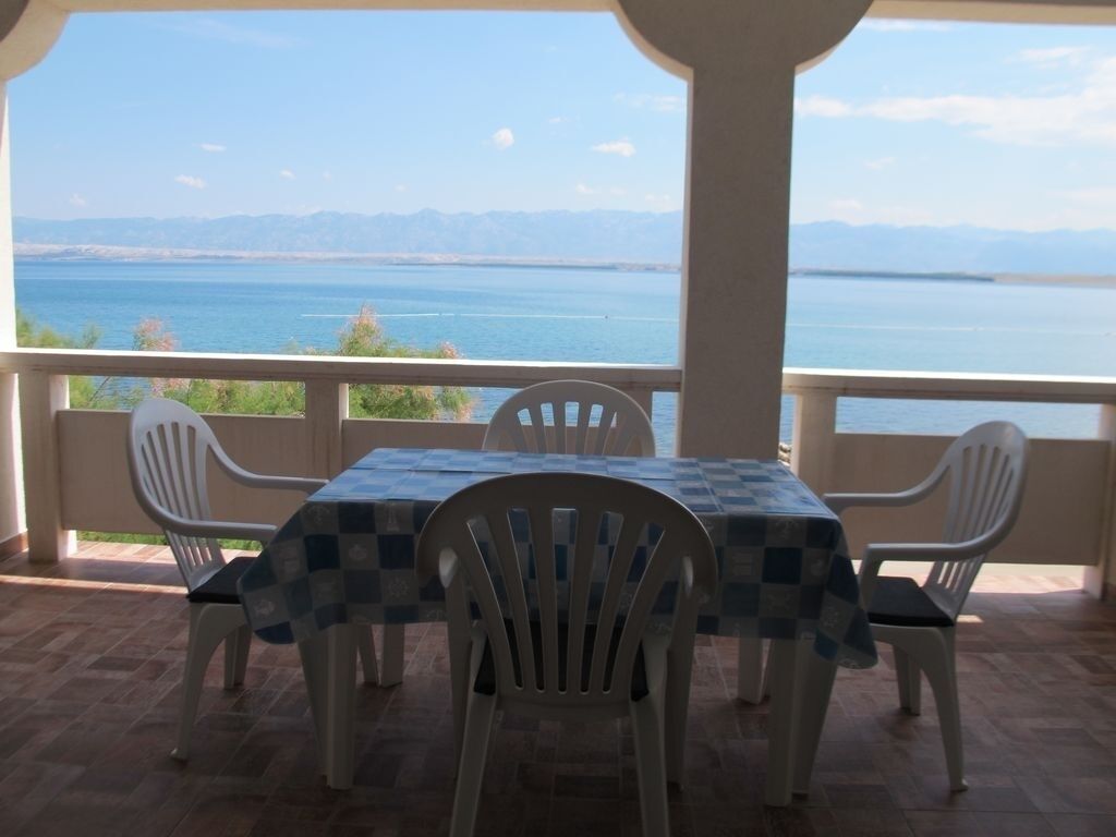 Eine Terrasse mit Tisch und Stühlen, mit Blick auf ein Gewässer und ferne Berge.