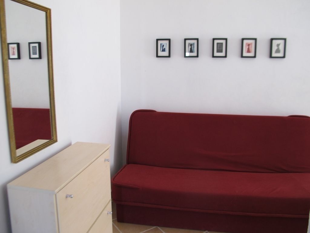 Een kamer met een rode bank, een houten kast en een muur met vijf ingelijste foto's.