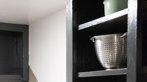 Una cocina con una paleta de colores blanco y negro, que incluye un lavaplatos, grifo, horno y estantes con vajilla y utensilios de cocina.