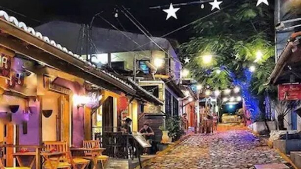 A cobblestone street with colorful paving, wooden furniture outside a building, and string lights overhead. - Pipa Ubaia Residence Apartments (Tibau do Sul)
