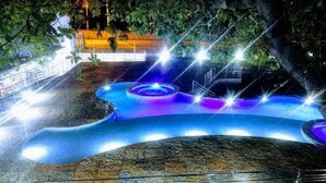 An outdoor swimming pool with a winding design, surrounded by a fence and illuminated by bright lights. - Pipa Ubaia Residence Apartments (Tibau do Sul)