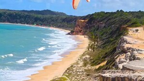 A coastal landscape with a beach, cliffs, and a paragliding activity. - Pipa Ubaia Residence Apartments (Tibau do Sul)