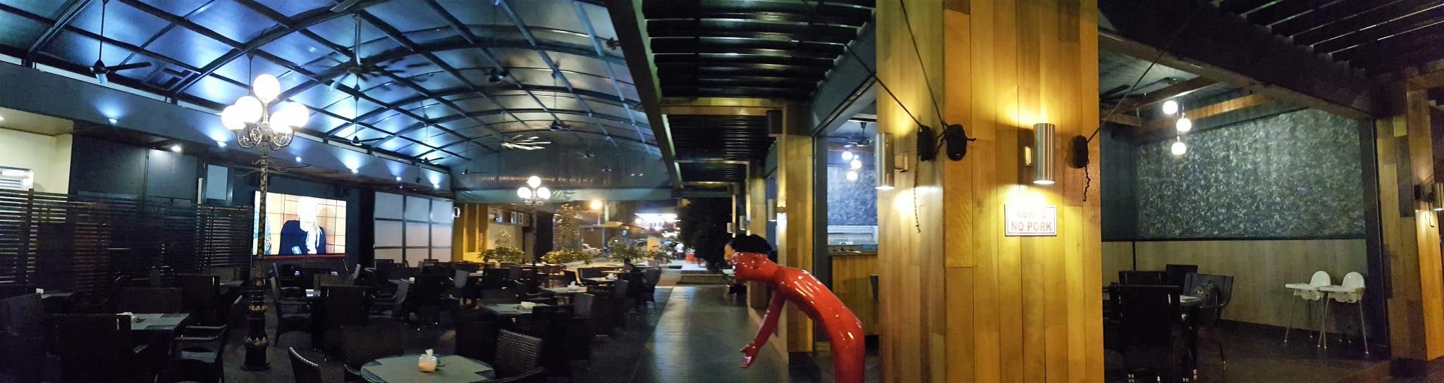 A restaurant with a high ceiling and a glass enclosure, tables and chairs arranged for dining, and a 'NO PORK' sign on the wall.