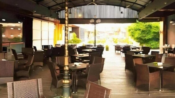 An indoor dining area with multiple tables and chairs, a central column, and a view of the outdoors. - D North Star Hotel Spa (Sandakan)