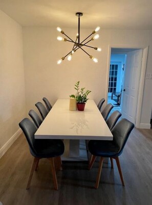 A dining area with a rectangular table, black chairs, a modern chandelier, and a potted plant. - 4 Bedroom House near the Hard Rock (Guitar Hotel) (Fort Lauderdale)