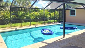 Ein Swimmingpool mit zwei blauen Luftmatratzen, umgeben von einer überdachten Fläche mit Blick auf üppiges Grün.