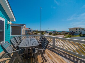 Una terraza de madera con una mesa y sillas, con vistas a una playa y edificios al fondo.