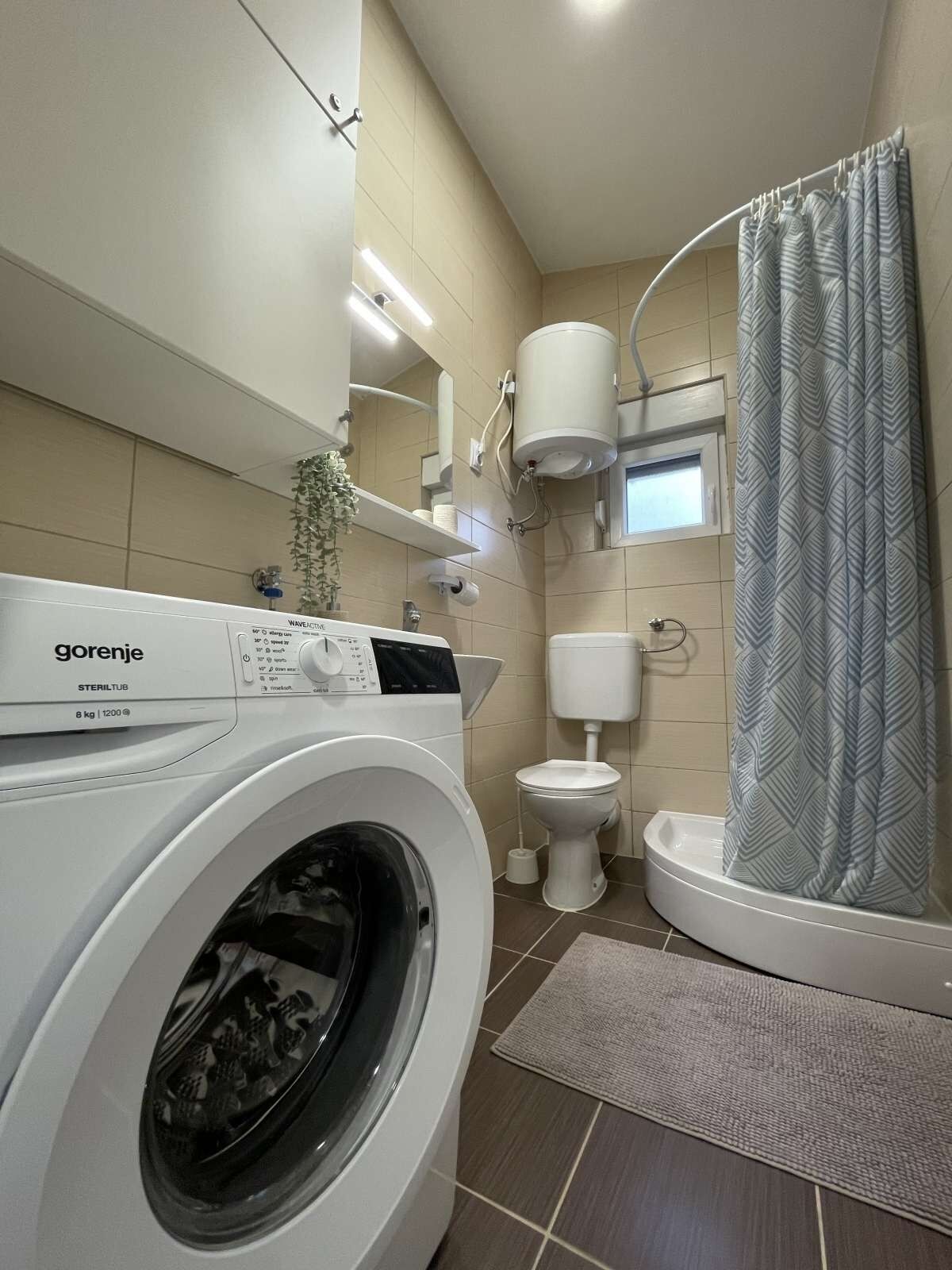 A compact bathroom with a washing machine, toilet, and shower.
