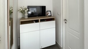 A hallway with a white door, a white cabinet with a television on top, and a small vase with flowers.