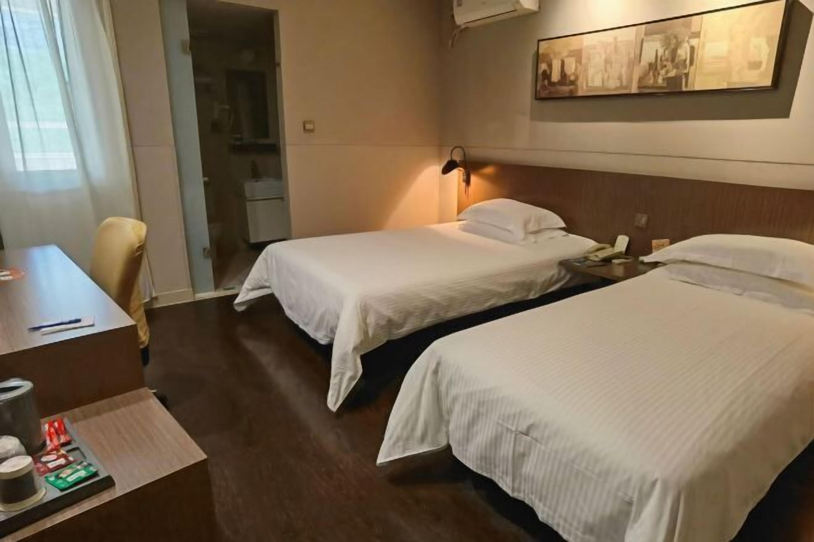 Ein Hotelzimmer mit zwei Einzelbetten, einem Schreibtisch mit Stuhl sowie einem kleinen Tisch mit Lampe.