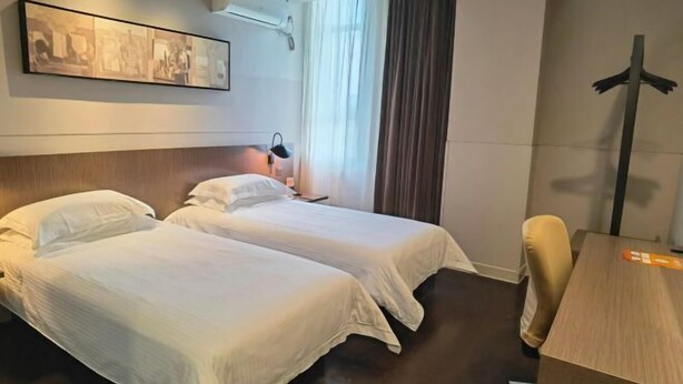 A hotel room with two beds, a desk, a chair, a window with curtains, and a wall-mounted air conditioner. - Jinjiang Inn Select (Shanghai Zhangjiang High-tech Park) (Shanghai)