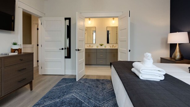 A hotel room with a bed, a dresser, a TV, and a bathroom visible through an open door. - Chic & Spacious Escape | East Nashville Stunner (Nashville)