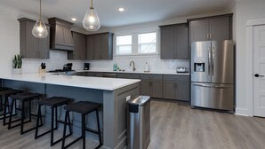 A modern kitchen with a large island, bar stools, stainless steel appliances, and pendant lighting. - Chic & Spacious Escape | East Nashville Stunner (Nashville)