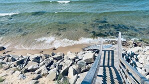 A wooden pier leading to a rocky beach with clear water.