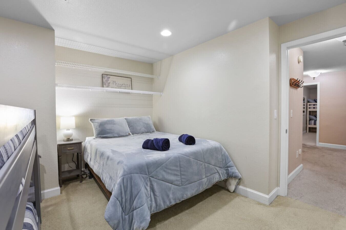 A bedroom with a bed, nightstand, and a wall-mounted shelf with a framed picture.
